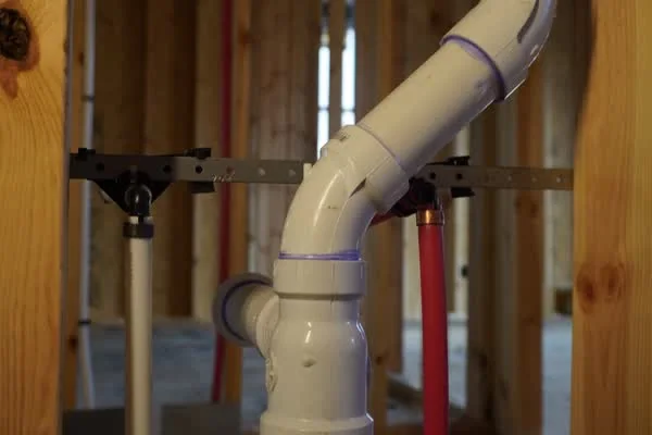 PVC drain-waste-vent piping and PEX supply lines supported on strut inside a framed interior