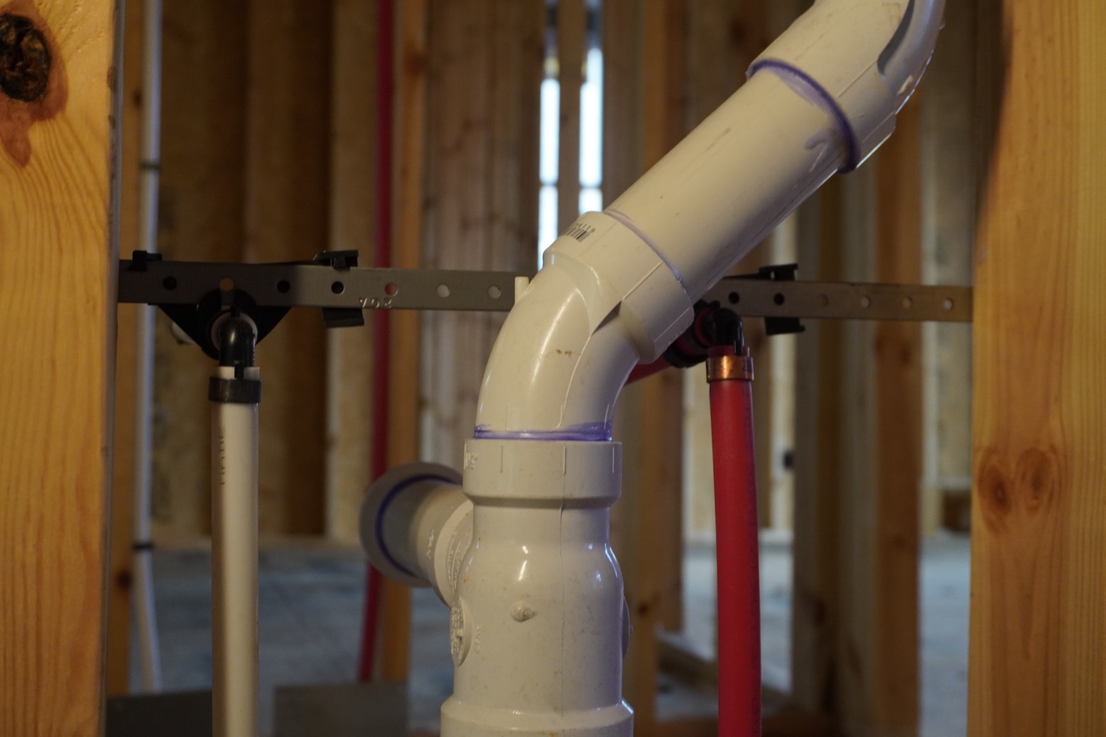 PVC drain-waste-vent fittings and a red PEX water line strapped between wall studs